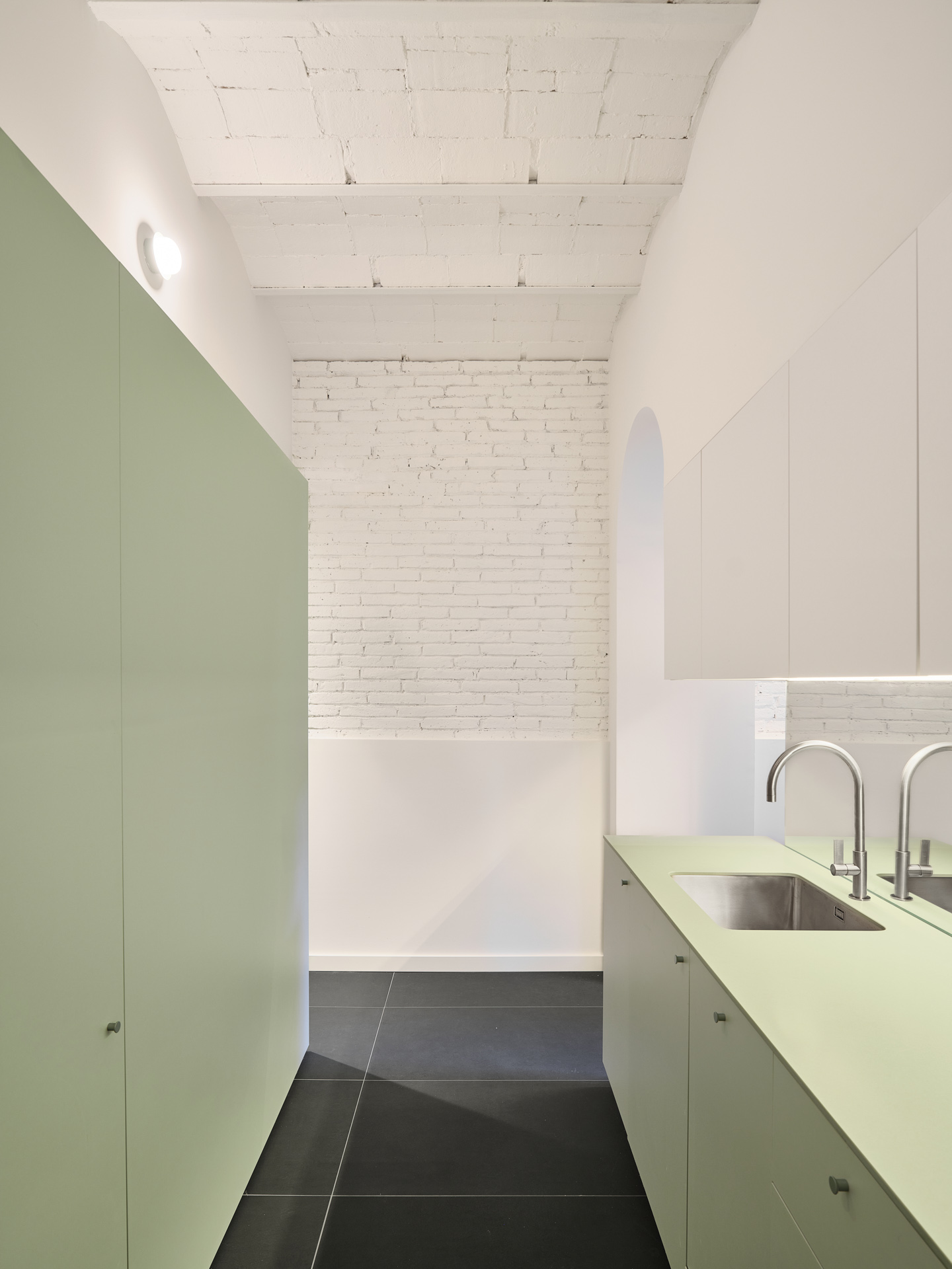 Kitchen in CRÜ’s “La Dolors” renovation, with soft green cabinetry, a double-sink island, whitewashed brick walls, and the restored exposed ceramic ceiling.